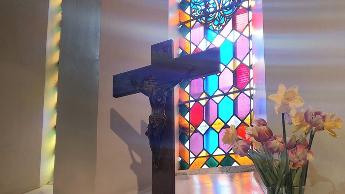 Ein Altar mit Kreuz, Kerzen und Blumen vor einem buntem Kirchenfenster