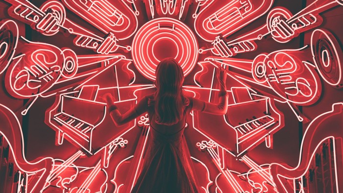 Eine Person steht unter einer kunstvollen, rot leuchtenden Neonwand aus Musikinstrumenten und Noten.