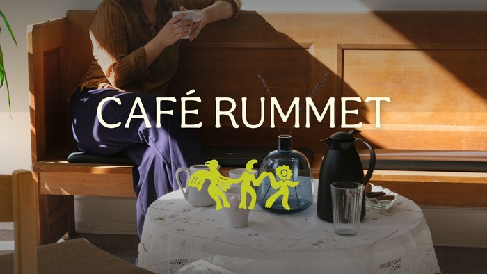 En hyggelig café med en person siddende ved et vindue, omgivet af farverige karakterer og kaffetilbehør.