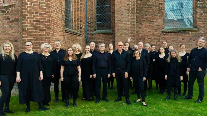 En gruppe af korister står sammen foran en murstenskirke.