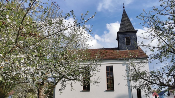 Weiße Kirche mit Turm und blühendem Baum davor
