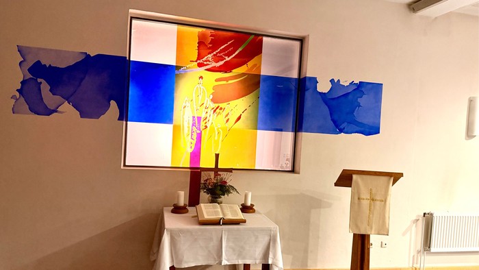 Ein ruhiger Altarbereich mit religiöser Kunst, Kerzen, einem Lesepult und einem geschmückten Tisch mit Büchern.