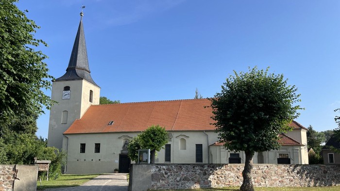 Idyllische Kirche mit hohem Kirchturm und rotem Ziegeldach, umgeben von üppigem Grün und einem Kopfsteinpflasterweg.