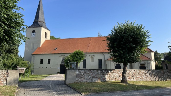Idyllische Kirche mit hohem Kirchturm und rotem Ziegeldach, umgeben von üppigem Grün und einem Kopfsteinpflasterweg.