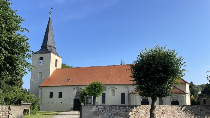 Idyllische Kirche mit hohem Kirchturm und rotem Ziegeldach, umgeben von üppigem Grün und einem Kopfsteinpflasterweg.