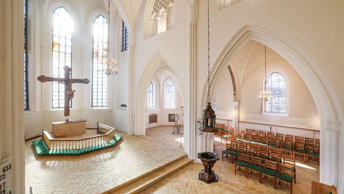 Elegant kirkeinteriør med træbænke, buede vinduer og et fremtrædende krucifiksalter.