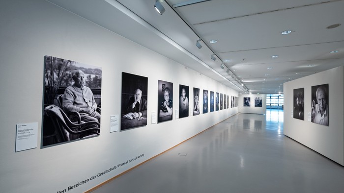 Ein Galeriegang mit einer Reihe von Schwarz-Weiß-Porträts, begleitet von Informationsschildern neben jedem Rahmen.