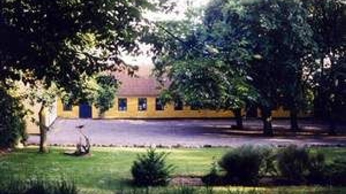 En lille gule hus med rødt tag og træer i en have