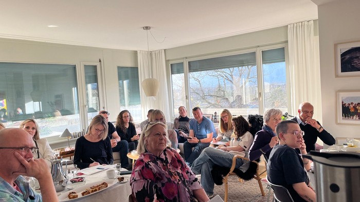 En gruppe mennesker, der socialiserer og nyder mad i en lys og rummelig indendørs omgivelse med store vinduer.