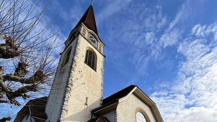 Moderne kirke med højt klokketårn mod en klar blå himmel og brostensgård.