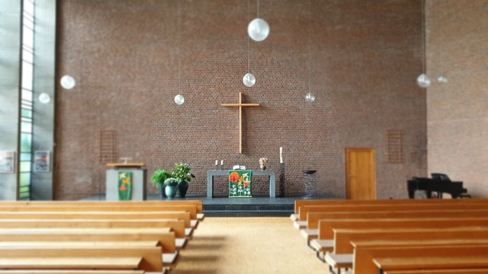 Leere Holzbänke in einer Kirche mit Kreuz und Altarraum