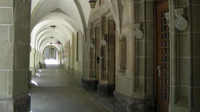 Ein langer, gewölbter Flur mit Holztüren und Wandleuchten.