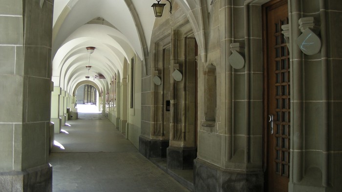 Ein langer, gewölbter Flur mit Holztüren und Wandleuchten.