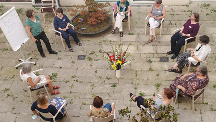 Eine Gruppe von Menschen sitzt im Kreis auf Stühlen im Freien und diskutiert.