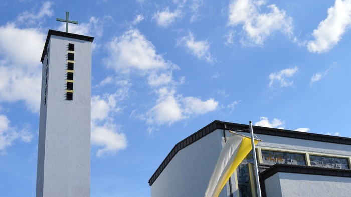 Moderne Kirche mit hohem Glockenturm und geschwungenem Eingangsüberdach unter einem strahlend blauen Himmel.