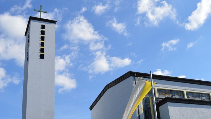 Moderne Kirche mit hohem Glockenturm und geschwungenem Eingangsüberdach unter einem strahlend blauen Himmel.