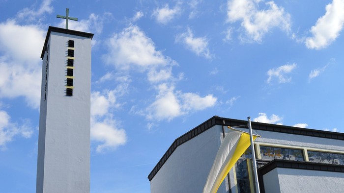 Moderne Kirche mit hohem Glockenturm und geschwungenem Eingangsüberdach unter einem strahlend blauen Himmel.