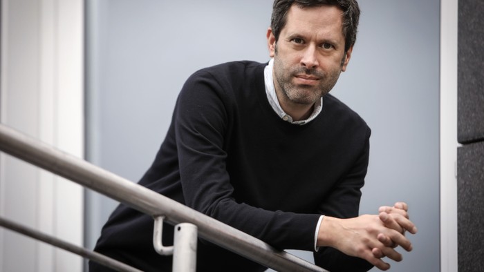 Mann lehnt an einem Metallgeländer und schaut zur Seite.