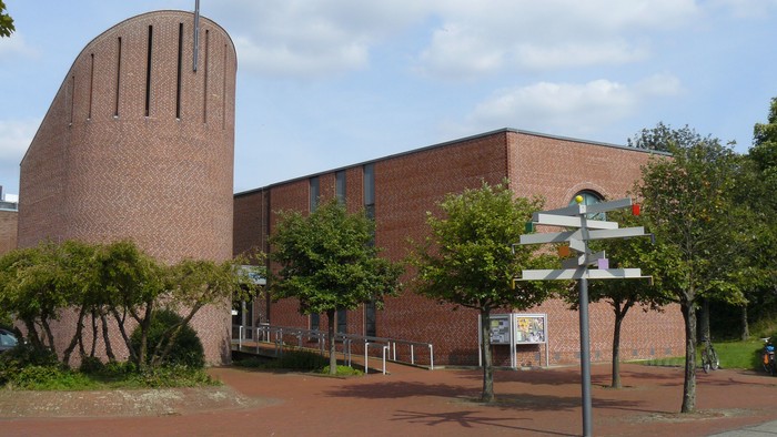 Ein Ziegelgebäude mit Kreuz und Bäumen vor einem klaren Himmel