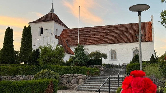 En hvid kirke med røde tagtag og en rød rose i forgrunden