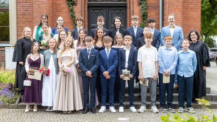 Gruppenfoto von Konfirmandinnen und Konfirmanden mit ihren beiden Pfarrerinnen und dem Jugendmitarbeiter vor der Kirche