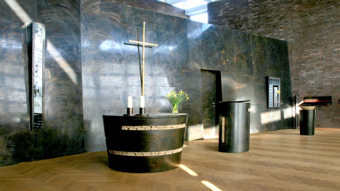 Ein moderner Kircheninnenraum mit Holzfußboden, schwarzem Altar und Kreuz.