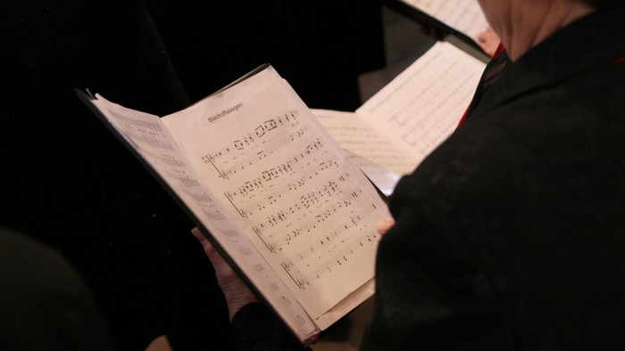 Eine ältere Dame hält ein aufgeschlagenes Liedblatt in der Hand. 