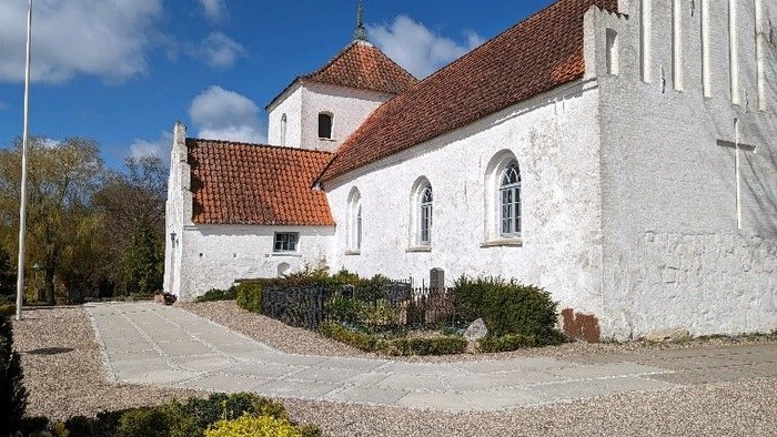 Et hvidt kirkebygning med røde tag og en smal vej fremfor.