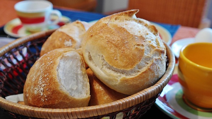 Frisch gebackene Brötchen in einem geflochtenen Korb, umgeben von bunten Tassen und Tellern.