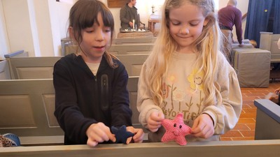 To børn leger med en lyserød tøjdyrsstjerne i en kirke.