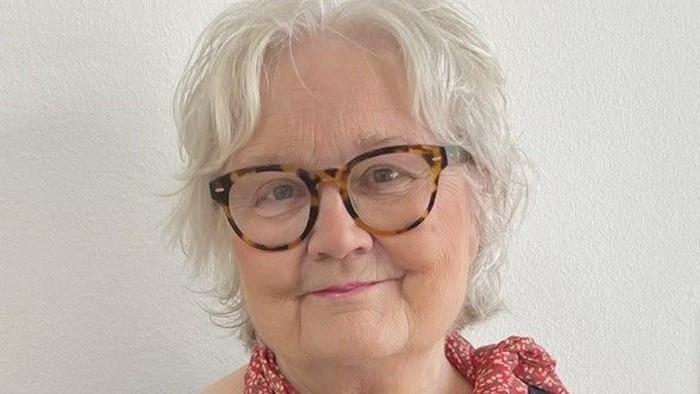 Ældre kvinde iført runde briller, sort top og et rødt mønstret tørklæde.