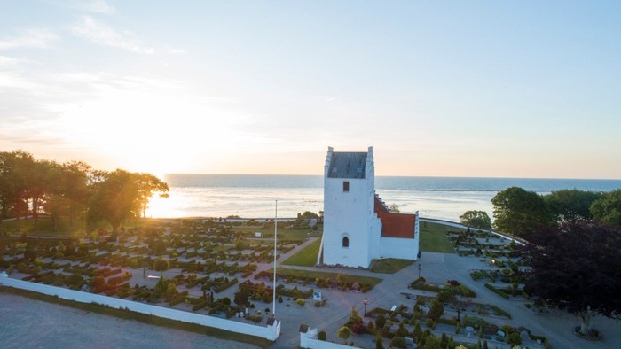 En hvid firkantet fyrtårn ved stranden med solnedgang i baggrunden