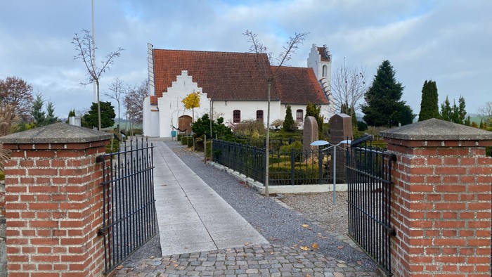En smuk kirke med røde tag og hvidt udseende, omgivet af en mur og en sti.