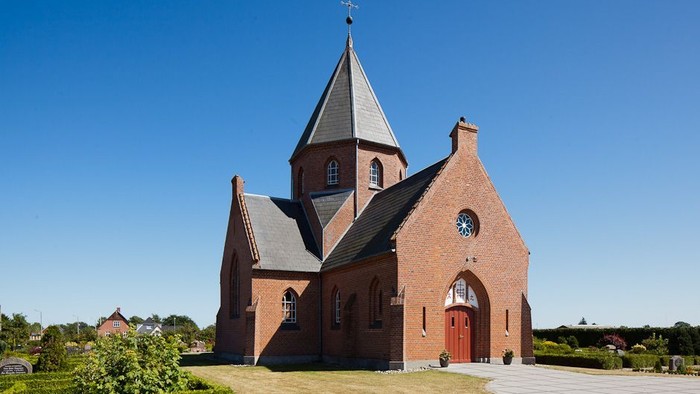 En rød murstenskirke med spiret og klokke.