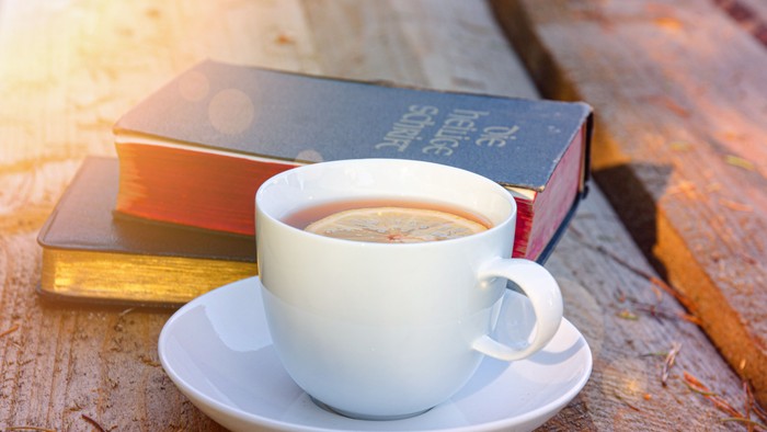 Ein Kaffeebecher auf einem Unterteller neben Büchern auf einem Holztisch