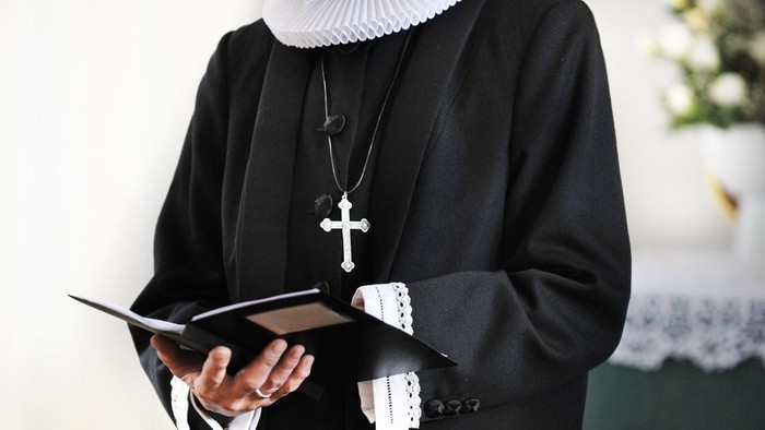 En præst holder en bog og bærer et kruzifix.