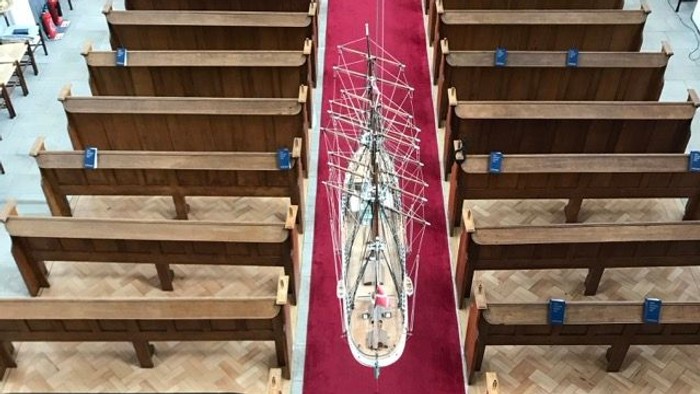 Et modelskib placeret ned gennem midtergangen i en kirke med træbænke på hver side.