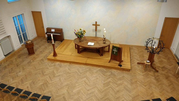 Modernes Kapelleninnenraum mit hölzernem Altar, Kirchenbänken und religiösen Symbolen wie einem Kreuz und Kerzenhaltern.