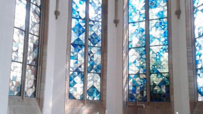 Ein ruhiger Kircheninnenraum mit hohen Buntglasfenstern und einem schlichten Altar, geschmückt mit Blumen und Kerzen.
