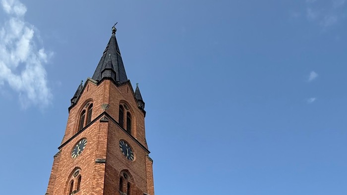 Große Ziegelkirche mit hohem Turm und Uhr unter blauem Himmel