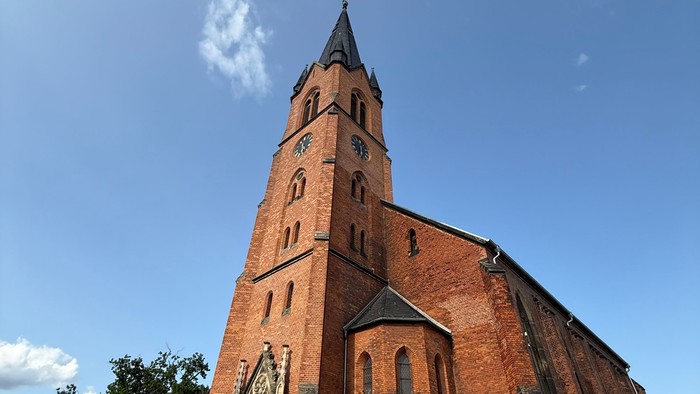 Große Ziegelkirche mit hohem Turm und Uhr unter blauem Himmel