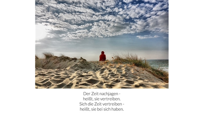 Frau sitzt auf einer Düne und schaut aufs Meer – darunter der Spruch: „Der Zeit nachjagen - heißt, sie vertreiben. Sich die Zeit vertreiben - heißt, sie bei sich haben.“