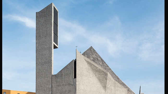 Moderne Kirche mit markantem Turm und spitzem Dach vor blauem Himmel