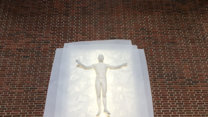 En lysbillede af en udstraket person monteret på en mur af røde teglsten.