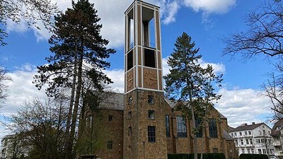 Eine Backsteinkirche mit einem hohen Glockenturm, umgeben von grünem Gras und hohen Bäumen.