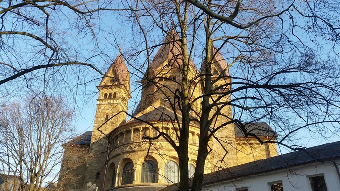 Historisches Gebäude mit Zwillingstürmen, eingerahmt von kahlen Bäumen unter klarem blauem Himmel.