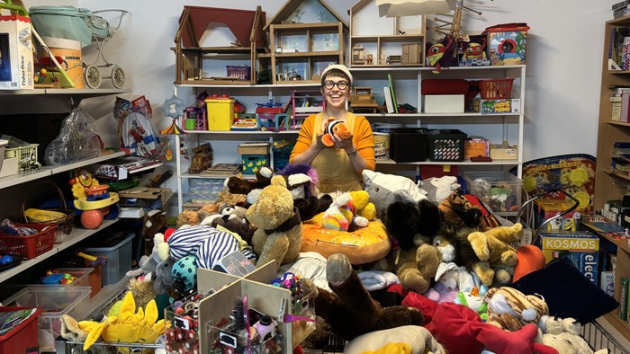 Eine Person steht zwischen einem unordentlichen Sammelsurium aus Stofftieren und Vintage-Spielzeugen auf Regalen.
