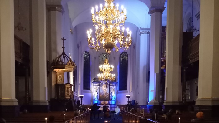 Elegant kirkeinteriør med store lysekroner, dæmpet belysning og lange træbænke, der fører hen til et alter.