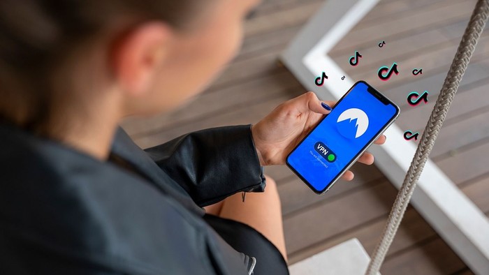 Eine Person, die ein Smartphone mit geöffneter TikTok-App benutzt, umgeben von schwebenden TikTok-Symbolen.