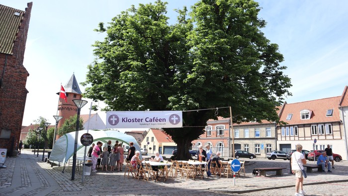 En stor træ i en byplads med café og folk der sidder udenfor